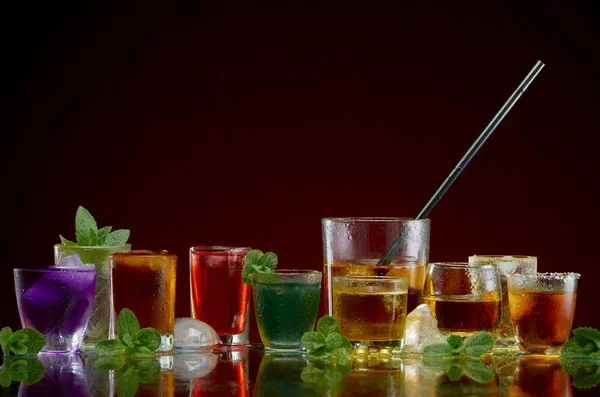 Different alcoholic drinks in clear glasses with ice and mint on red background — Stock Photo, Image