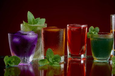 Various alcoholic cocktails in clear glasses with ice and mint on a red background clipart