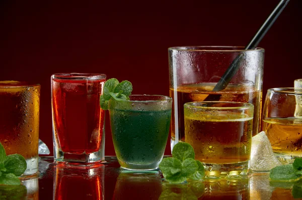 Diverse alcoholische cocktails in heldere glazen met ijs en munt op een rode achtergrond — Stockfoto