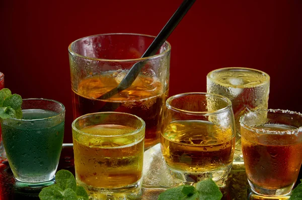 Очки с различными алкогольными напитками со льдом и мятой на красном фоне — стоковое фото