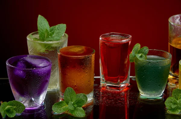 Glasses with various alcoholic drinks with ice and mint on red background — Stock Photo, Image