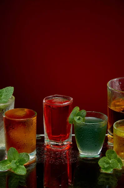Gekleurde alcoholische dranken met ijs en Mint op rode achtergrond — Stockfoto