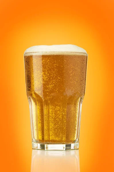 Rempli de bière légère fraîche verre facetté isolé sur orange — Photo