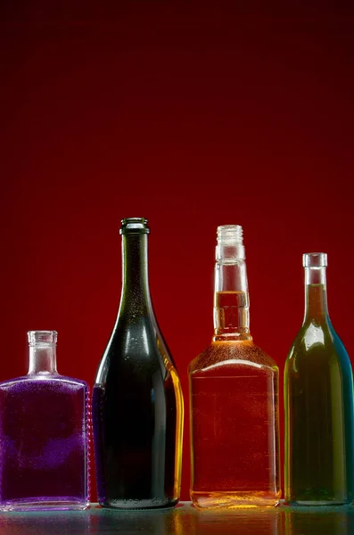 Diferentes bebidas alcohólicas en botellas transparentes sobre fondo rojo — Foto de Stock