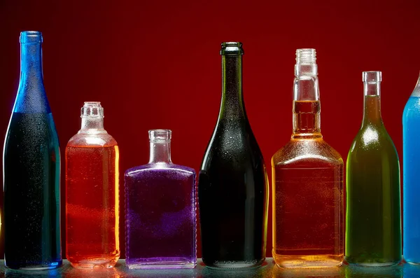 Различные алкогольные напитки в прозрачных бутылках на красном фоне — стоковое фото
