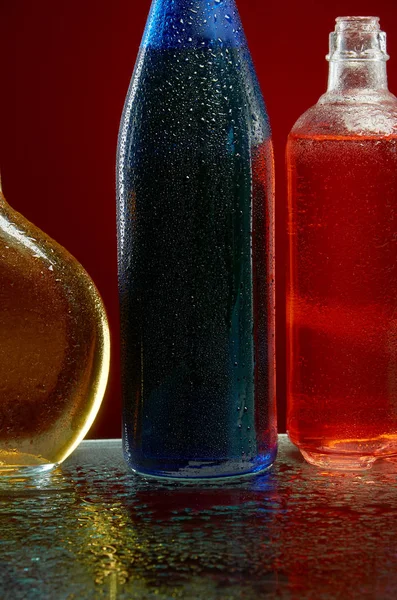 Alcohol flessen in water druppels op rode achtergrond — Stockfoto