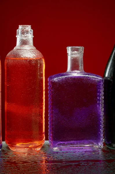 Botellas de alcohol en gotas de agua sobre fondo rojo — Foto de Stock