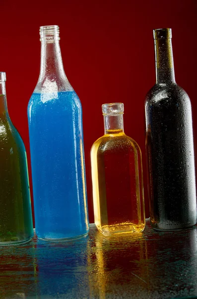 Botellas de alcohol en gotas de agua sobre fondo rojo — Foto de Stock