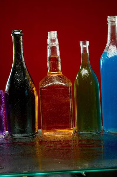 Botellas de alcohol en gotas de agua sobre fondo rojo —  Fotos de Stock