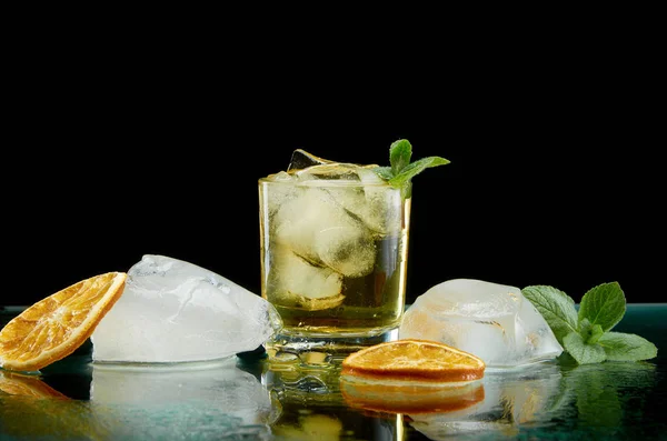 Холодный алкогольный коктейль со льдом оранжевый и свежие травы на черном фоне — стоковое фото