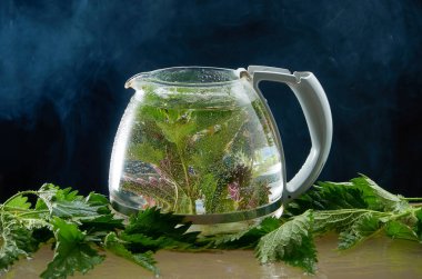 Siyah bir arka planda ısırgan yaprakları ve duman ile tıbbi Isırgan Çayı çaydanlık