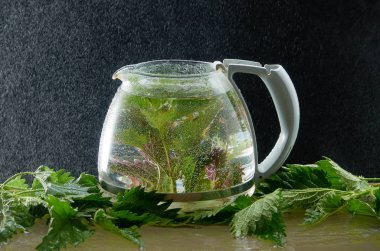 Siyah bir arka planda ısırgan yaprakları ve su tozu ile tıbbi Isırgan Çayı çaydanlık