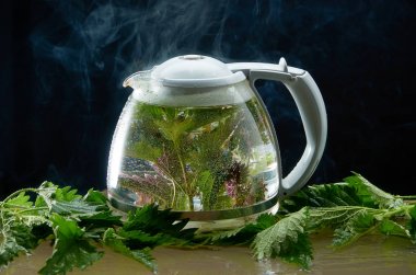 Siyah bir arka planda ısırgan yaprakları ve duman ile tıbbi Isırgan Çayı çaydanlık