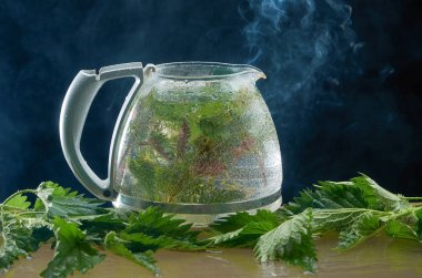 Siyah bir arka planda ısırgan yaprakları ve duman ile tıbbi Isırgan Çayı çaydanlık