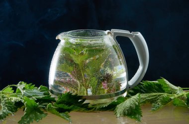 Siyah bir arka planda ısırgan yaprakları ve duman ile tıbbi Isırgan Çayı çaydanlık