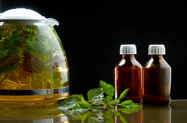 Tea teapot of fresh nettle and nettle leaves in a medical environment on a black background — Stock Photo, Image