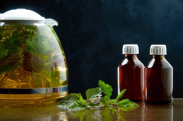 Teiera di tè di ortica fresca e foglie di ortica in un ambiente medico su uno sfondo nero — Foto Stock