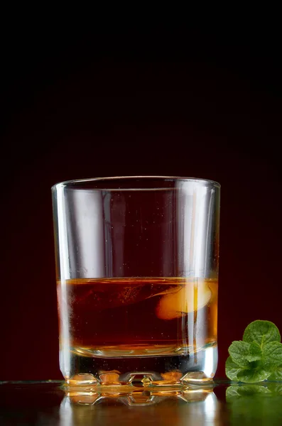 玻璃与酒精在透明玻璃与冰和薄荷的红色背景 — 图库照片