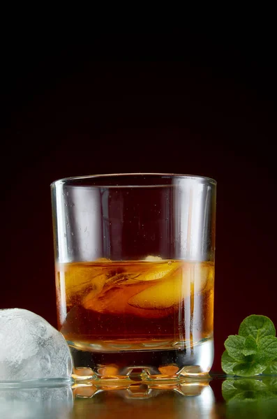 Glass with alcohol in a transparent glass with ice and mint on a red background — Stock Photo, Image