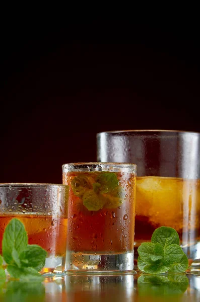 Alcoholische drank in glazen met ijs en munt op rode achtergrond — Stockfoto