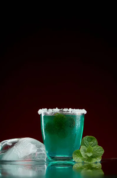 Sklo s originálním alkoholovým nápojem s mátou a ledem na červeném pozadí — Stock fotografie