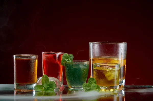 Alkoholhaltig dryck med is och mynta i en ljus rök på den röda bakgrunden — Stockfoto