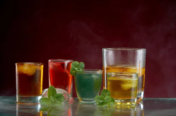 Different alcoholic cocktails with ice and mint with light smoke on a red background — Stock Photo, Image