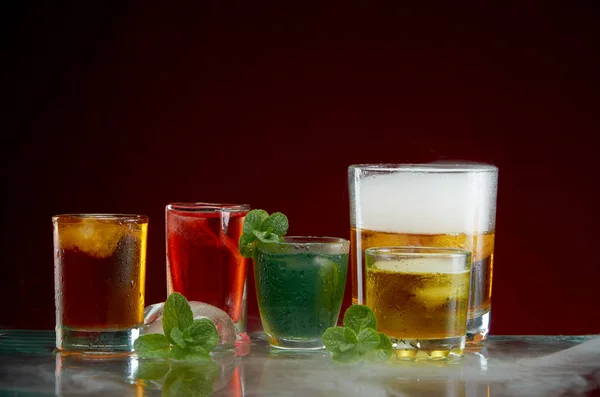 Olika alkoholhaltiga cocktails med is och mynta med ljus rök på en röd bakgrund — Stockfoto