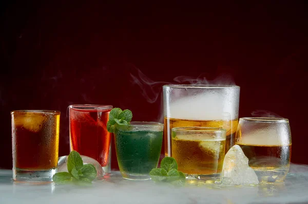 Verschillende alcoholische cocktails met ijs en munt met lichte rook op een rode achtergrond — Stockfoto