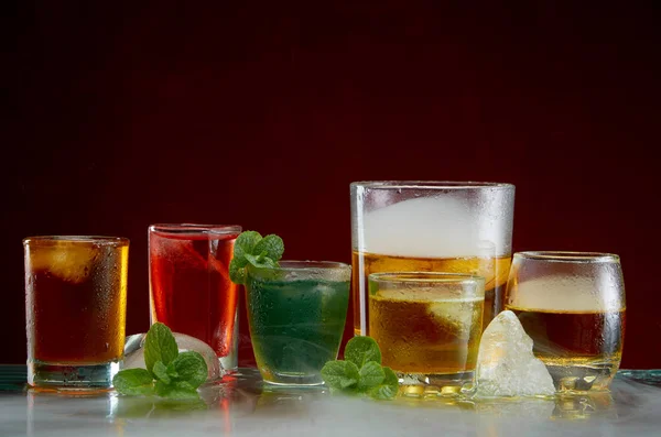 Különböző alkoholos koktélok jéggel és menta enyhe füsttel, vörös háttérben — Stock Fotó
