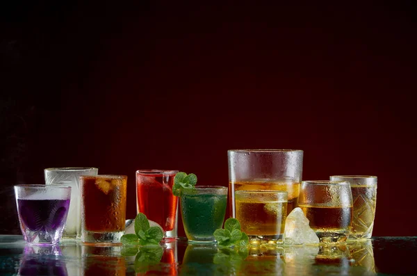 Színes fúvósszeptettre alkoholtartalmú italok átlátszó Üvegpoharak a jég és a menta a füst vörös alapon — Stock Fotó