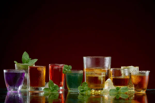 Different alcoholic drinks in clear glasses with ice and mint on red background — Stock Photo, Image