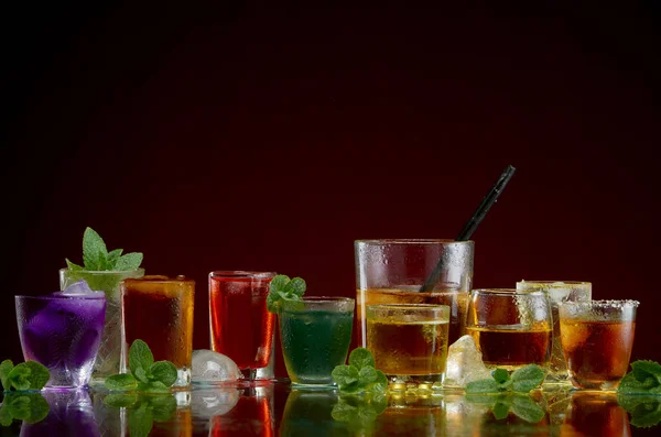 Different alcoholic drinks in clear glasses with ice and mint on red background — Stock Photo, Image