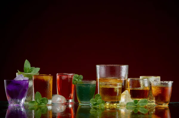 Verschiedene alkoholische Getränke in klaren Gläsern mit Eis und Minze auf rotem Hintergrund — Stockfoto