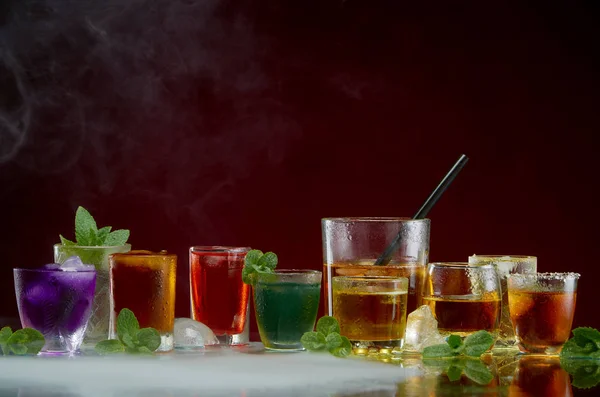 Color septet of alcoholic beverages in transparent glass glasses with ice and mint in smoke on a red background — Stock Photo, Image