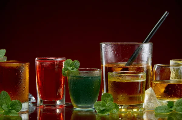 Diverse alcoholische cocktails in heldere glazen met ijs en munt op een rode achtergrond — Stockfoto