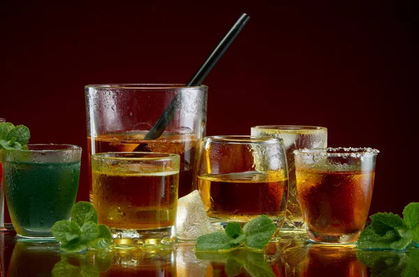 Különböző alkoholtartalmú koktélok jéggel és menta tiszta üvegben, piros alapon — Stock Fotó