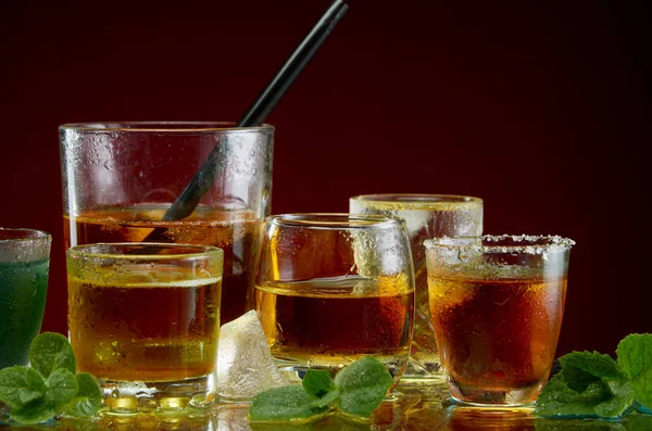 Various alcoholic cocktails in clear glasses with ice and mint on a red background — Stock Photo, Image