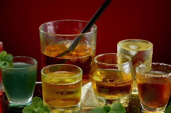Glazen met diverse alcoholische dranken met ijs en munt op rode achtergrond — Stockfoto
