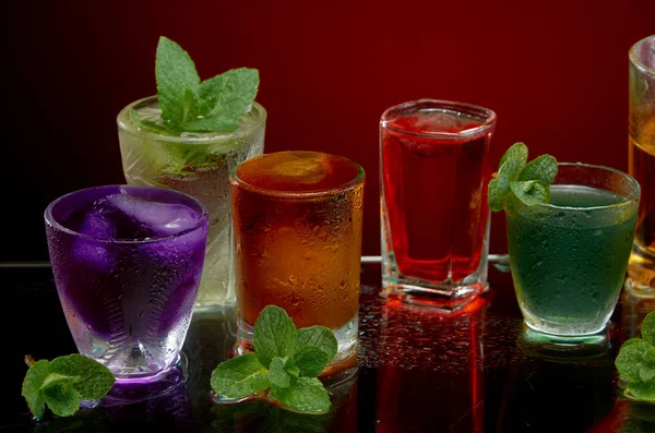 Färgade alkoholhaltiga drycker med is och mynta på röd bakgrund — Stockfoto