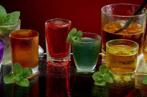 Színes alkoholos italok jéggel és menta vörös háttérrel — Stock Fotó
