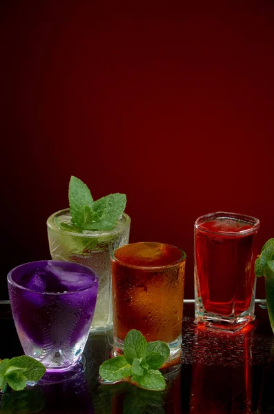 Boissons alcoolisées colorées avec glace et menthe sur fond rouge — Photo