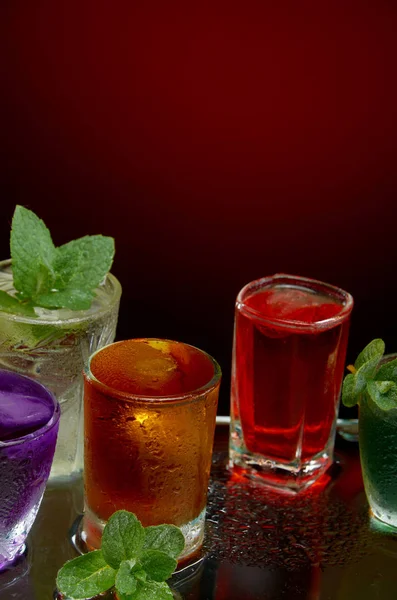 Barevné alkoholické nápoje s ledem a mátou na červeném pozadí — Stock fotografie
