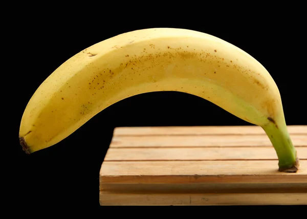 Amarelo maduro banana manchado de pé na placa em um fundo preto — Fotografia de Stock