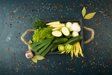 Taş üzerindeki kutudaki sebzeler koyu bir arka plan. Genç Otlar Soğan Sarımsak Yeşil Fasulye Sarı Mısır Kabak Parlak Baharatlar Koyu Dokulu Arka Plan Üzerinde Halat Kolları ile Ahşap Bir Kutu bulunmaktadır.