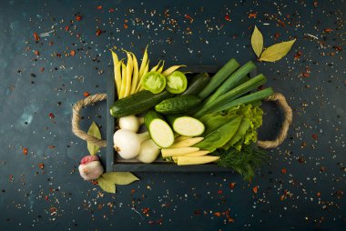 Taş üzerindeki kutudaki sebzeler koyu bir arka plan. Genç Otlar Soğan Sarımsak Yeşil Fasulye Sarı Mısır Kabak Parlak Baharatlar Koyu Dokulu Arka Plan Üzerinde Halat Kolları ile Ahşap Bir Kutu bulunmaktadır.