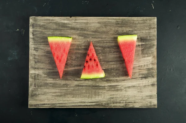 Watermeloen op de achtergrond. Drie stukjes rijp sappige watermeloen op een houten plank. — Stockfoto