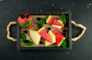 Kavun Karpuz Böğürtlen Nane ve Arka Planda Kutuda Bir Bardak Meyve Suyu. Olgun Karpuz Sulu Kavun Böğürtlen ve Nane ile Karanlık Bir Arka Plan Üzerine Bir Kokteyl ile Ahşap Bir Kutu da vardır.