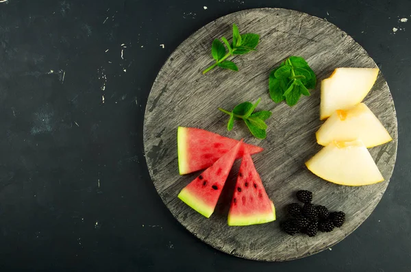 MELON WATERMELON BLACKBERRY Y MINT ON THE BACKGROUND. TRES PIEZAS DE RIPE WATERMELON JUICY MELON CON RIPE BLACKBERRIES MINT LIE EN UNA BORRERA DE MADERA EN UNA DONDA . — Foto de Stock