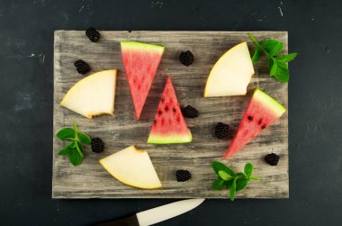 Kavun Karpuz Böğürtlen Ve Arka Planda Nane. Olgun Blackberries Nane ile Olgun Karpuz Sulu Kavun Üç Adet Karanlık Bir Arka Plan Üzerine Ahşap Bir Tahta Üzerinde Bir Bıçak ile Yalan.